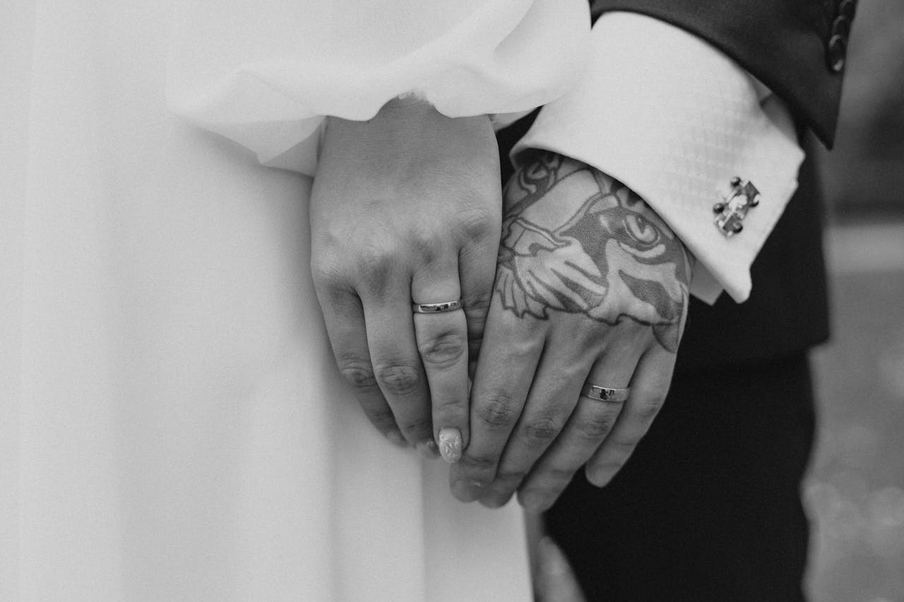 services-02 Close-up shot of married couple holding hands with rings, showcasing tattoos.